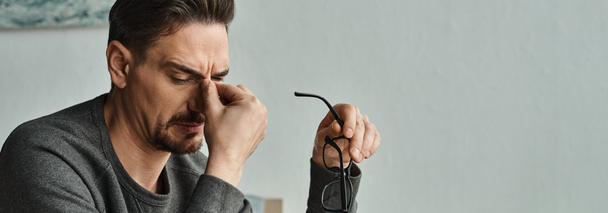 stresszes szakállas férfi alkalmi viselet szemüveg és megható szemek munka után otthon, banner - Fotó, kép