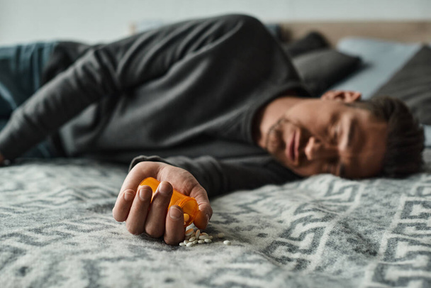 blurred shot of bearded man sleeping on bed near bottle with medication, - Photo, Image