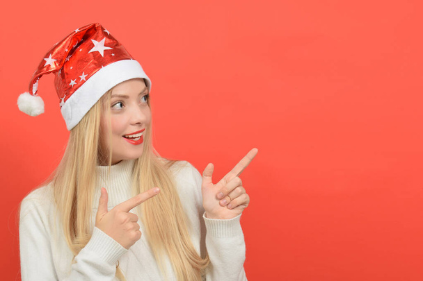 Šťastná mladá žena v Santa Claus klobouk ukazuje na kopírovat prostor na červeném pozadí - Fotografie, Obrázek