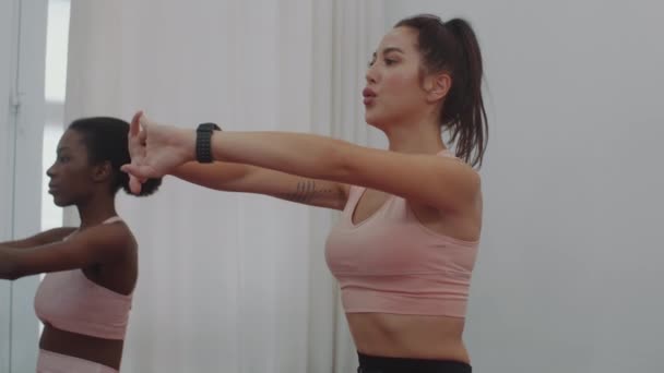 Medium slowmo van Kaukasische en Afro-Amerikaanse sportvrouwen training in stretching klasse of het doen van ademhalingsoefeningen binnen - Video