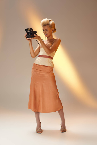 stilvolles Mädchen in ihren 20ern im Korsett-Outfit, das Foto mit Retro-Kamera im grauen Hintergrund macht - Foto, Bild