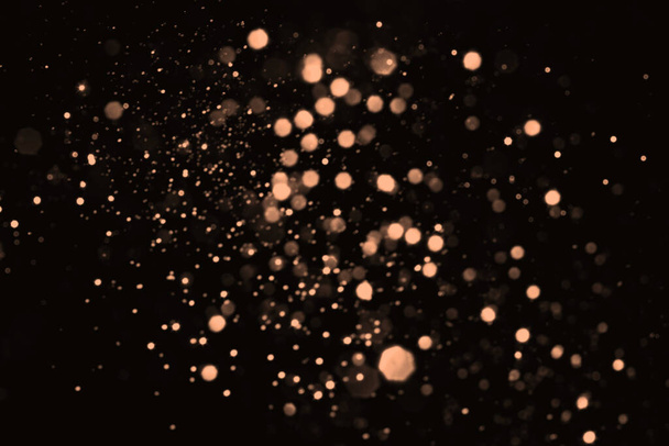 Peach Fuzz verschwimmt abstrakte Bokeh-Lichter auf schwarzem Hintergrund. Schneeglitzernde Glitzersternchen zum Feiern - Foto, Bild