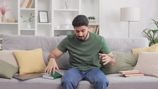 Indiánský student cítí stres z domácí práce, zatímco sedí na gauči a obklopen knihami. Millennial chlap v ležérní oblečení dotýkání hlavy s rukama během obtíží před zkouškami. - Záběry, video
