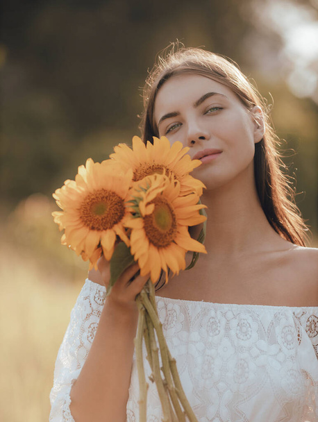Close up portrait of attractive young woman holding sunflowers. Nature and outdoor concept. Summer time. Horizontal layout. Beautiful face. - Photo, Image