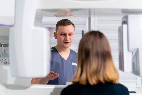 ein männlicher Arzt konsultiert eine Patientin in der Nähe des 3D-Scangeräts vor Beginn des Eingriffs in einer Klinik für plastische Chirurgie oder Zahnheilkunde - Foto, Bild