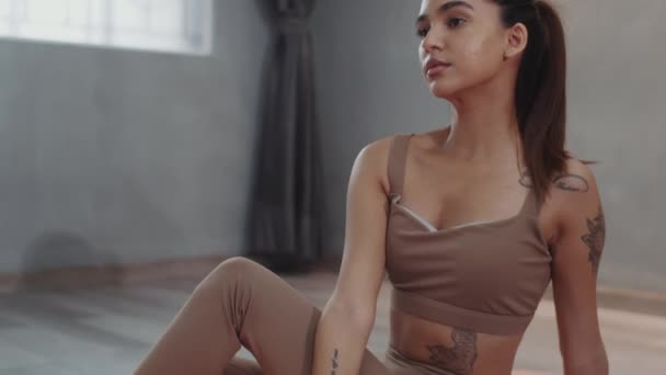 Tilt up portret van jonge Aziatische sportvrouw met tatoeages op lichaam en armen glimlachen op de camera zitten op de vloer in fitness studio - Video