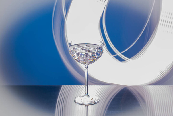 Közelkép egy pohár alkoholról, jégkockákkal, fehér és kék absztrakt háttérrel. - Fotó, kép