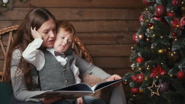 Äiti ja söpö poika lukemassa satukirjaa joulukuusen alla illalla - Materiaali, video