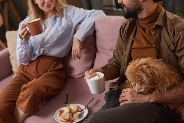 High angle shot of young man and woman spending morning together sitting on sofa in living room with their dog having breakfast and chatting - Foto, Imagen