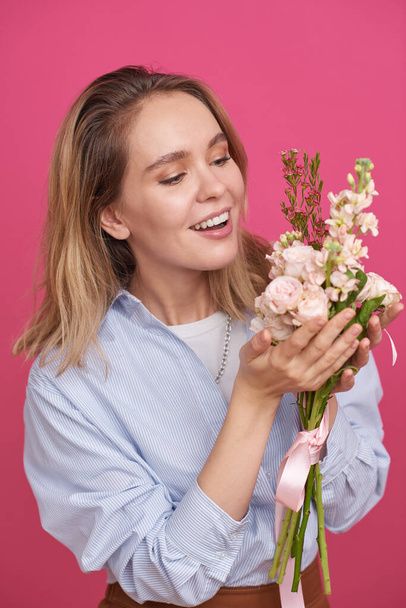 Vertical medium portrait of attractive young woman standing against pink wall background holding beautiful flower bouquet - Fotó, kép