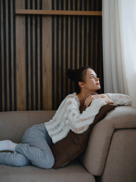 Nainen villapaita ja kotihousut rentouttava makaa sohvalla kotona, viihtyisä vapaapäivä mukavasti, todellinen elämäntapa hymyillen. Laadukas kuva - Valokuva, kuva