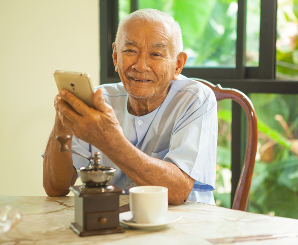 Šťastný asijských starší muž pomocí mobilního telefonu v domě - Fotografie, Obrázek