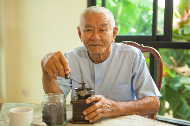Азиатский пожилой человек со старинной кофемолкой
 - Фото, изображение