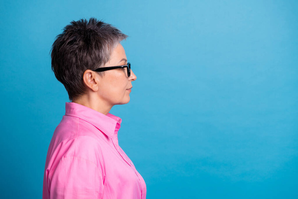 Side profile photo of serious confident woman dressed pink shirt in glasses look at offer empty space isolated on blue color background. - Foto, Imagem
