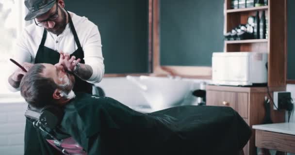 Baard, scheerschuim en een kapper met een man in een stoel als klant voor luxe of professionele service. Salon, scheer- of kapper en een persoon die het gezicht van een klant verzorgt met een minora mes. - Video