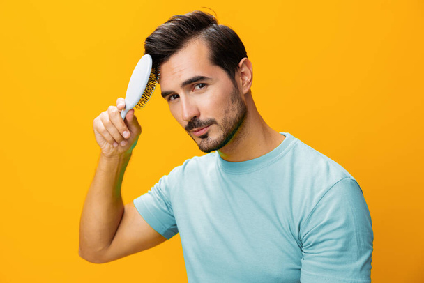 Портрет чоловіка на фоні зачіски красива студія краси випадання волосся крупним планом перукарський догляд за гребінцем, який тримає бороду розчісуючи жовте усміхнене обличчя - Фото, зображення