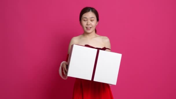 Nagranie azjatyckiej kobiety noszącej świąteczny materiał trzymającej pudełko z prezentem szczęśliwie z różowym tłem na plecach - Materiał filmowy, wideo