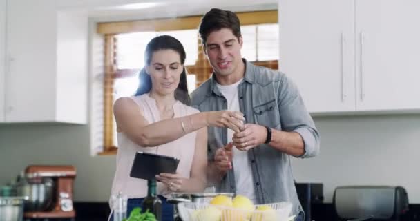 Happy couple, cooking in kitchen with tablet and help, healthy food for nutrition and happiness in marriage. Diet, man helping woman with meal prep and dinner in home with online recipe or tutorial - Footage, Video