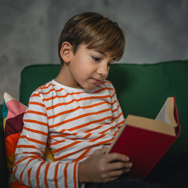 Ένα καυκάσιο αγόρι στο σπίτι διαβάζει ένα βιβλίο στο μπροστινό μέρος της βραδιάς αντιγραφή χώρο πραγματικό άνθρωποι εκπαίδευση έννοια - Φωτογραφία, εικόνα