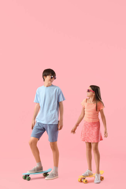 ピンクの背景にスケートボードを持つかわいい少女と彼女の兄 - 写真・画像