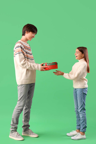 Hermano con caja de regalo saludando a su linda hermana sobre fondo verde - Foto, imagen