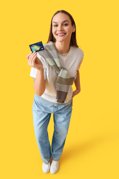 Young woman with credit card on yellow background - Фото, изображение