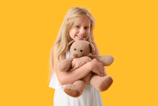 Schattig klein meisje met pluche teddybeer op gele achtergrond - Foto, afbeelding