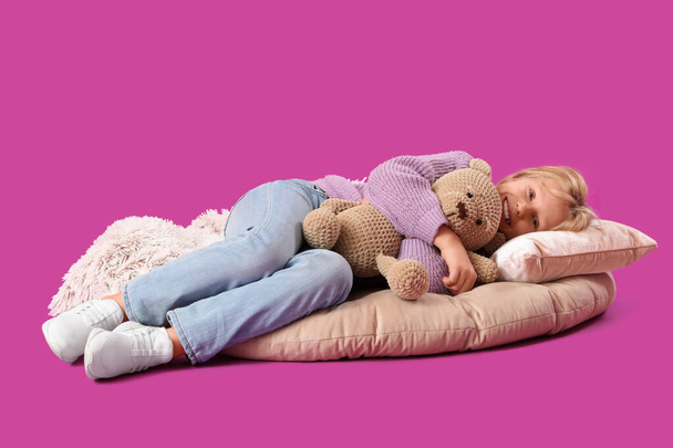 Petite fille mignonne avec ours en peluche couché sur fond violet - Photo, image