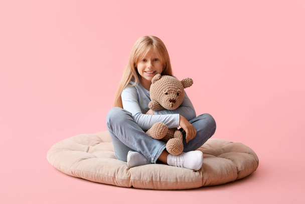 Χαριτωμένο κοριτσάκι με βελούδινο αρκουδάκι κάθεται σε ροζ φόντο - Φωτογραφία, εικόνα