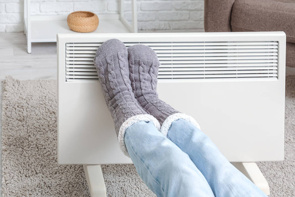 Fiatal nő meleg téli zokniban az elektromos fűtés közelében. A fűtési idény fogalma - Fotó, kép