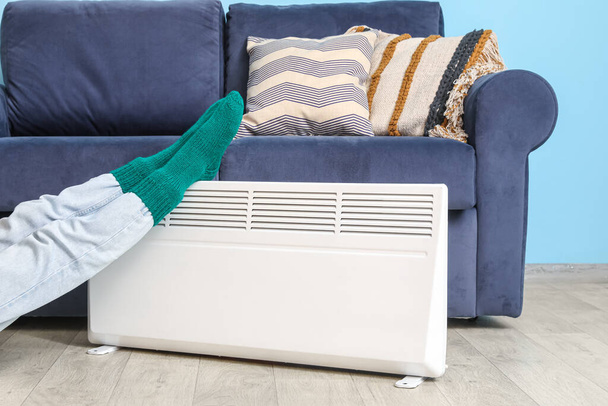 Mujer en calcetines calientes cerca de calentador eléctrico en casa. Concepto de temporada de calefacción - Foto, Imagen