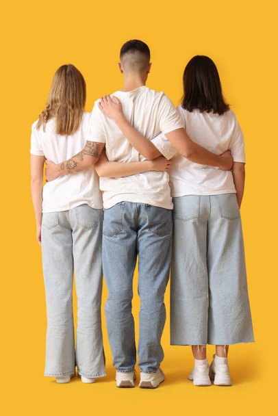 Młodzi ludzie w stylowych dżinsach ściskający się na żółtym tle, widok z tyłu - Zdjęcie, obraz