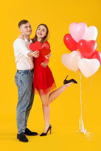 黄色の背景に紙のハートと風船を持つ素敵なカップル. バレンタインデーのお祝い - 写真・画像