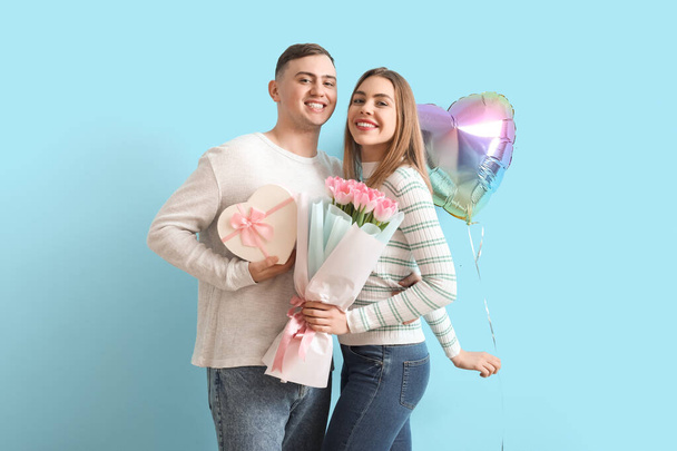 Schönes Paar mit herzförmigem Ballon und Blumenstrauß auf blauem Hintergrund. Valentinstag-Feier - Foto, Bild