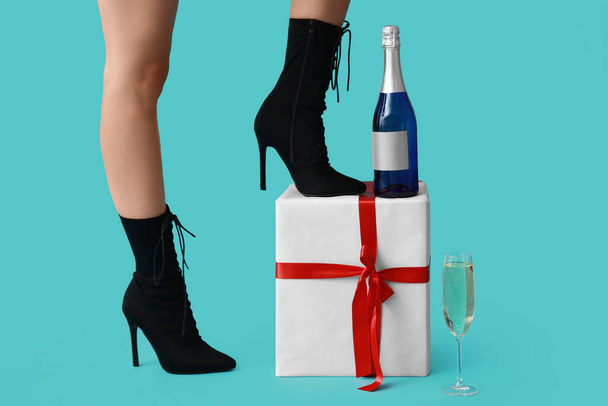 Женские ноги в туфлях на высоком каблуке с бутылкой шампанского и подарком на голубом фоне. Новогодняя вечеринка - Фото, изображение