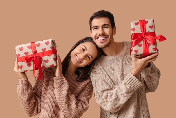 Красивая молодая пара с подарочными коробками на коричневом фоне. Празднование Дня Святого Валентина - Фото, изображение