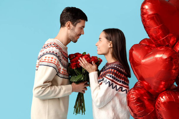 Beautiful young couple with bouquet of red roses and heart shaped air balloons on blue background. Valentine's day celebration - Photo, Image