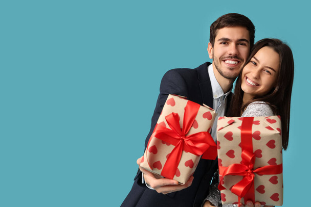 Beautiful young couple with gift boxes on blue background. Valentine's day celebration - Photo, Image