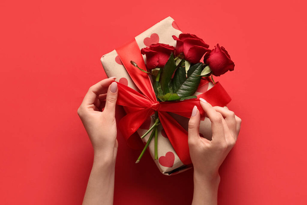 Женские руки с красивыми розами и подарочной коробкой на красном фоне. Празднование Дня Святого Валентина - Фото, изображение