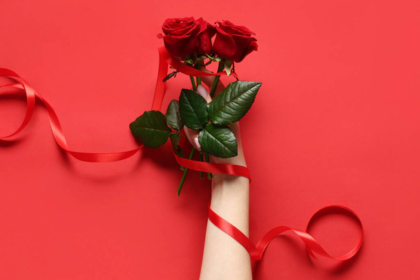 Female hand with beautiful red roses on color background. Valentine's day celebration - Photo, Image