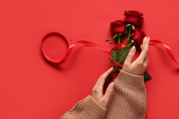 Female hands with beautiful red roses on color background. Valentine's day celebration - Photo, Image