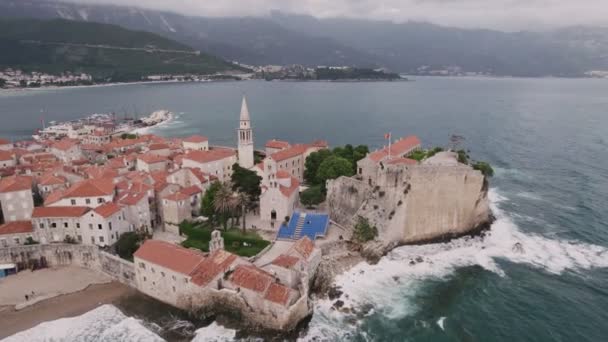 Oude middeleeuwse stenen stadshuizen met rode daken en kerkklokkentorens. Budva is het centrum van toerisme in Montenegro en een zomervakantie bestemming. Luchtfoto drone stadsgezicht in Montenegro. - Video