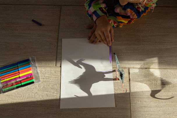 rastros infantiles contrastando sombras de dinosaurio de juguete con rotulador. dibujo de un estudiante de primaria, ideas creativas para la creatividad. Actividades interesantes para los niños. juego de luz y sombra - Foto, Imagen