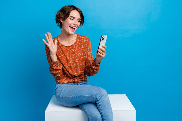 Photo portrait of attractive young woman sit wave hand video call gadget dressed stylish brown clothes isolated on blue color background. - Foto, Imagen
