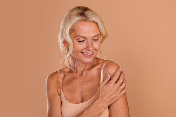 Photo of dreamy cheerful middle age woman wear bikini arm touching shoulder smiling isolated beige color background. - Fotoğraf, Görsel