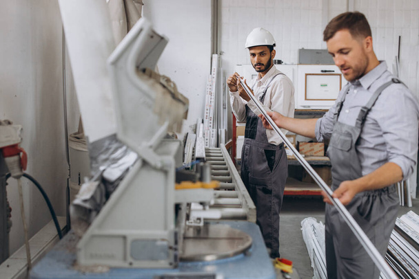 Ein internationales Team, zwei Arbeiter arbeiten an einer Maschine in einer Fabrik für PVC-Fenster und -Türen - Foto, Bild