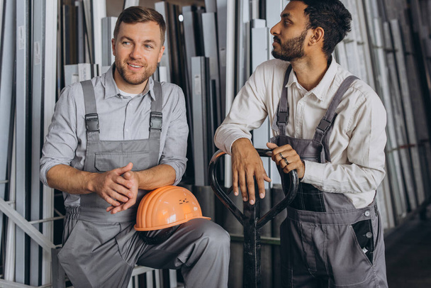 Retrato de dos trabajadores internacionales con sombreros que toman un descanso del trabajo y descansan hablando entre sí en un fondo de fábrica con espacio para copiar - Foto, imagen