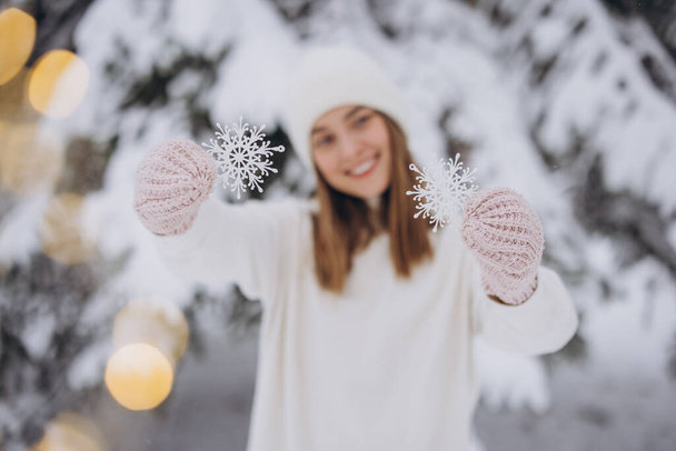 Happy woman in knitted white clothes holding snowflakes on the background of a snowy pine tree in winter - Photo, Image