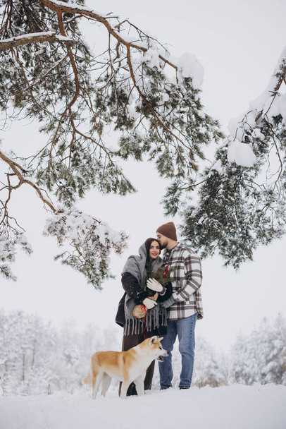 Ευτυχισμένο νεαρό ζευγάρι με σκύλο ακίτα στο δάσος την ημέρα του χειμώνα - Φωτογραφία, εικόνα