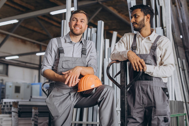 Портрет двух иностранных рабочих в касках, отдыхающих, разговаривающих друг с другом на фабричном фоне с копировальным пространством - Фото, изображение